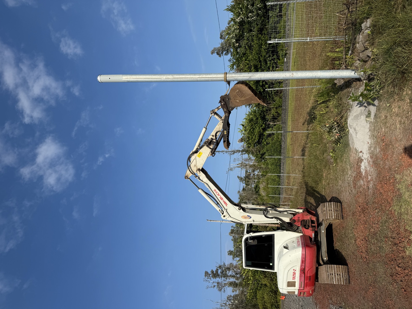 J Boys Services excavator on Big Island job site with red dirt and blue sky